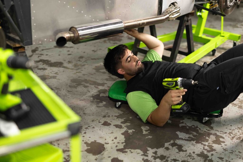 JMC36415-64 Mecánico usando una llave de impacto Kroner acostado bajo el escape de un auto